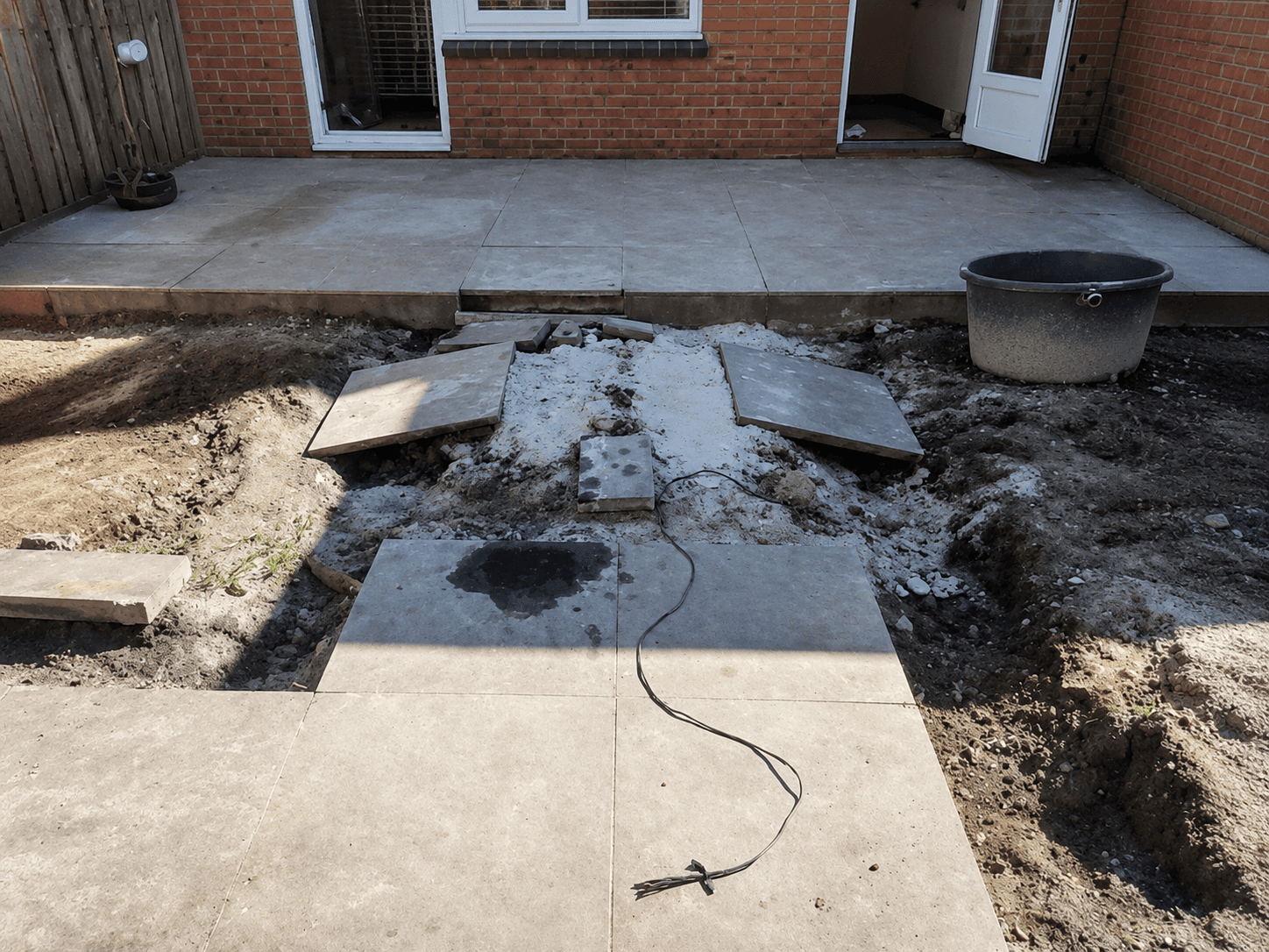 Backyard during groundworks, with excavated subsoil and lifted slabs.