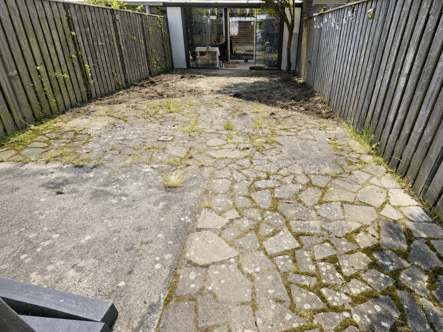 Narrow city garden before the renovation, with broken flagstones covered in moss and weeds.